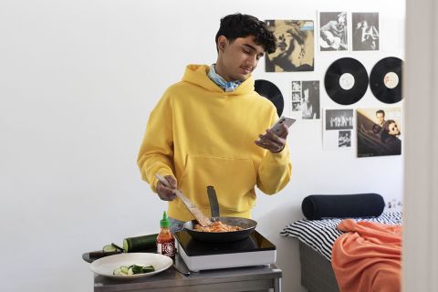 Feelia Ruokakaupan brändikuva, jossa henkilö valmistaa ruokaa keittolevyllä makuuhuoneessa ja samalla katsoo puhelintaan.