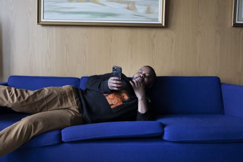 Tummaihoinen henkilö (Seksikäs-Suklaa) makoilee sohvalla kännykän kanssa.