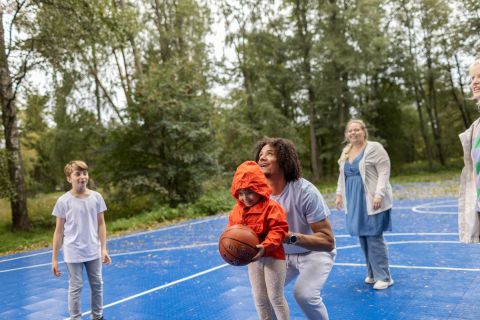 Work in Finlandin ja Business Finlandin brändikuva, jossa useampi aikuinen ja lapsi ovat pelaamassa koripalloa ulkona.