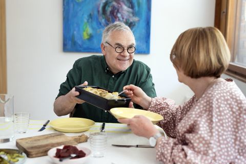 Feelia Ruokakaupan brändikuva, jossa kaksi henkilö istuvat pöydän ääressä, toinen heistä ojentaa toiselle valmista uuniruokaa.