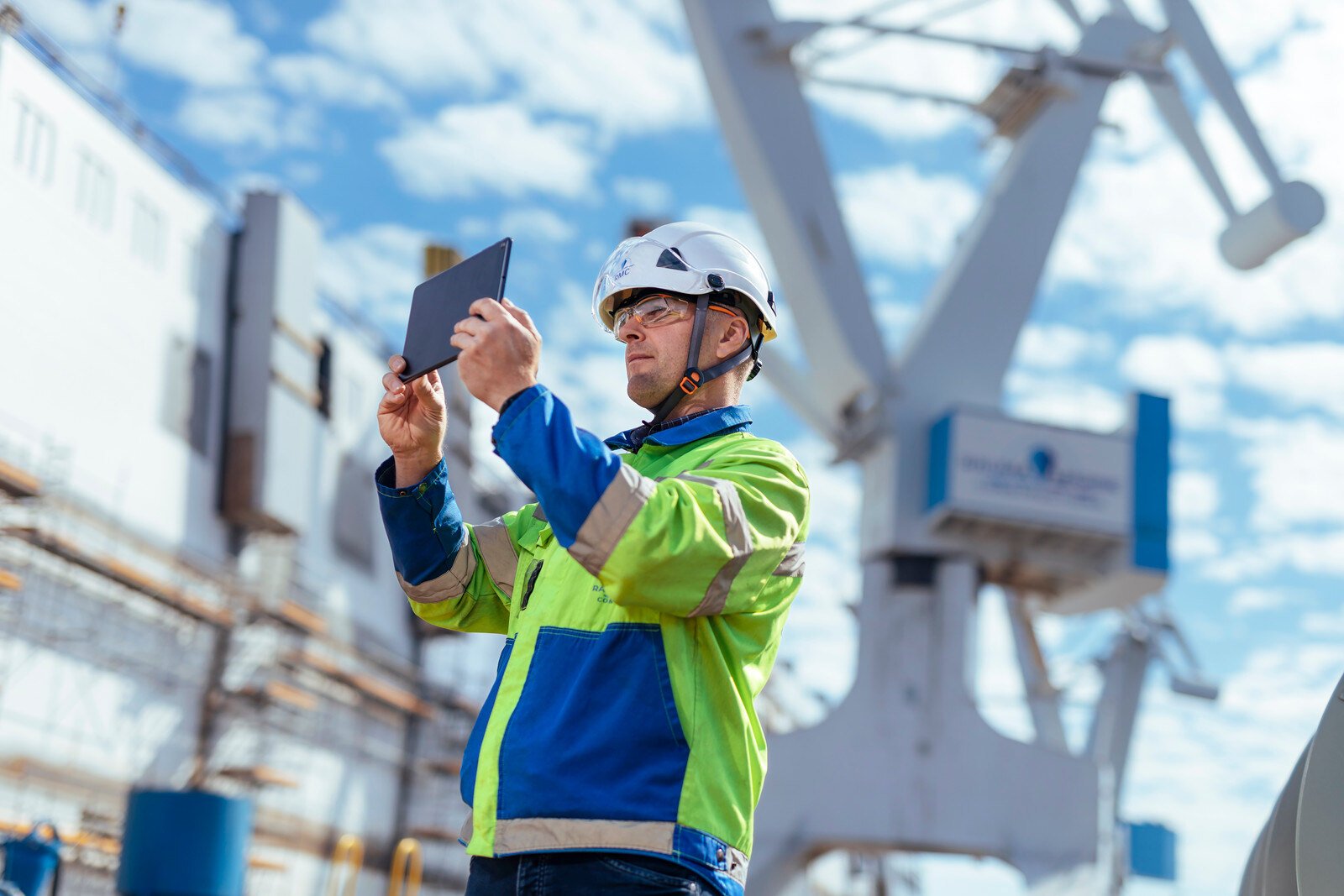 Henkilö on telakalla ja hänellä on kädessään padi ja päällään turvavartusteita.