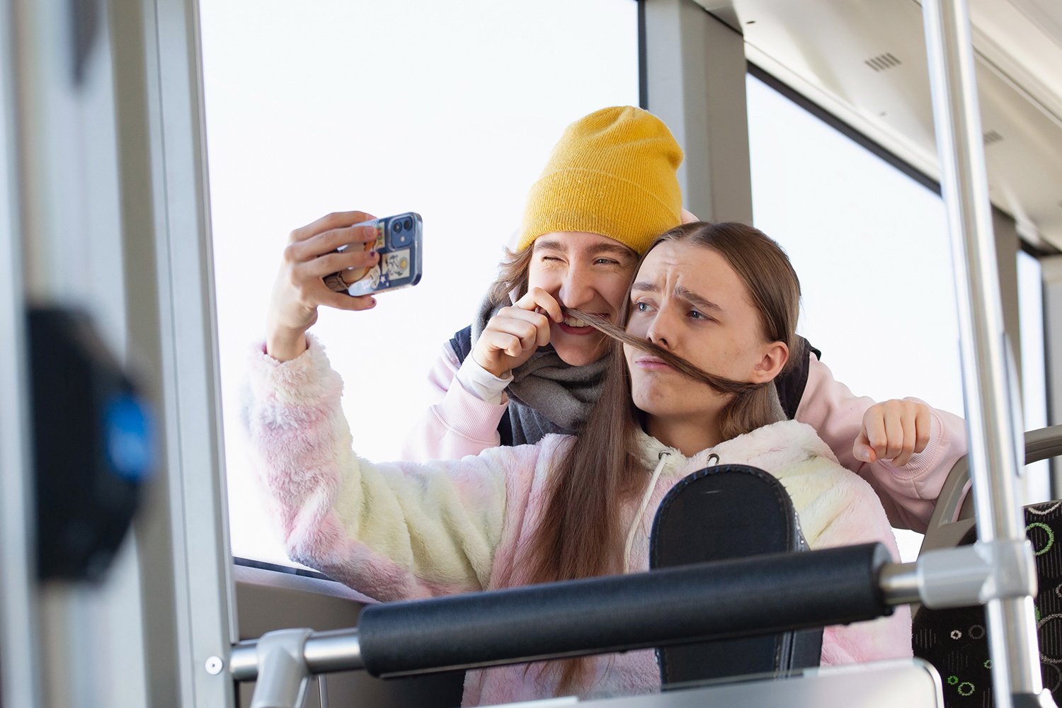 Kaksi henkilöä ottavat yhteiskuvaa bussissa.