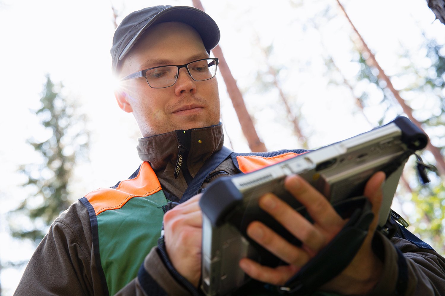Henkilö käyttää digitaalista laitetta metsässä.