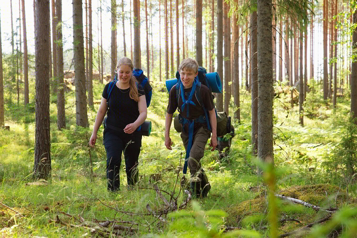 Kaksi henkilöä kävelemässä metsässä reput selässä.