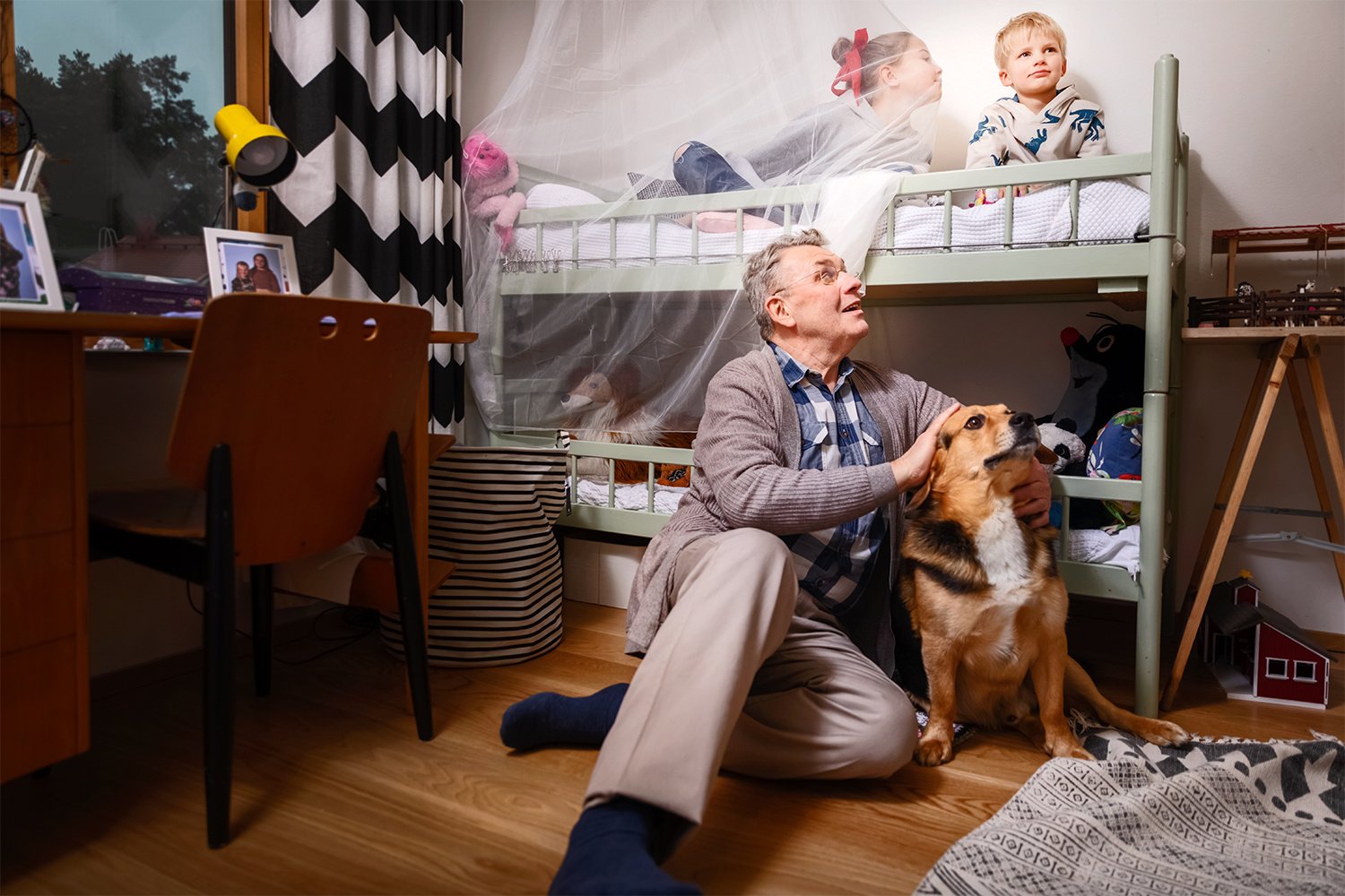 Kaksi lasta kerrossängyssä sekä aikuinen ja koira lattialla.