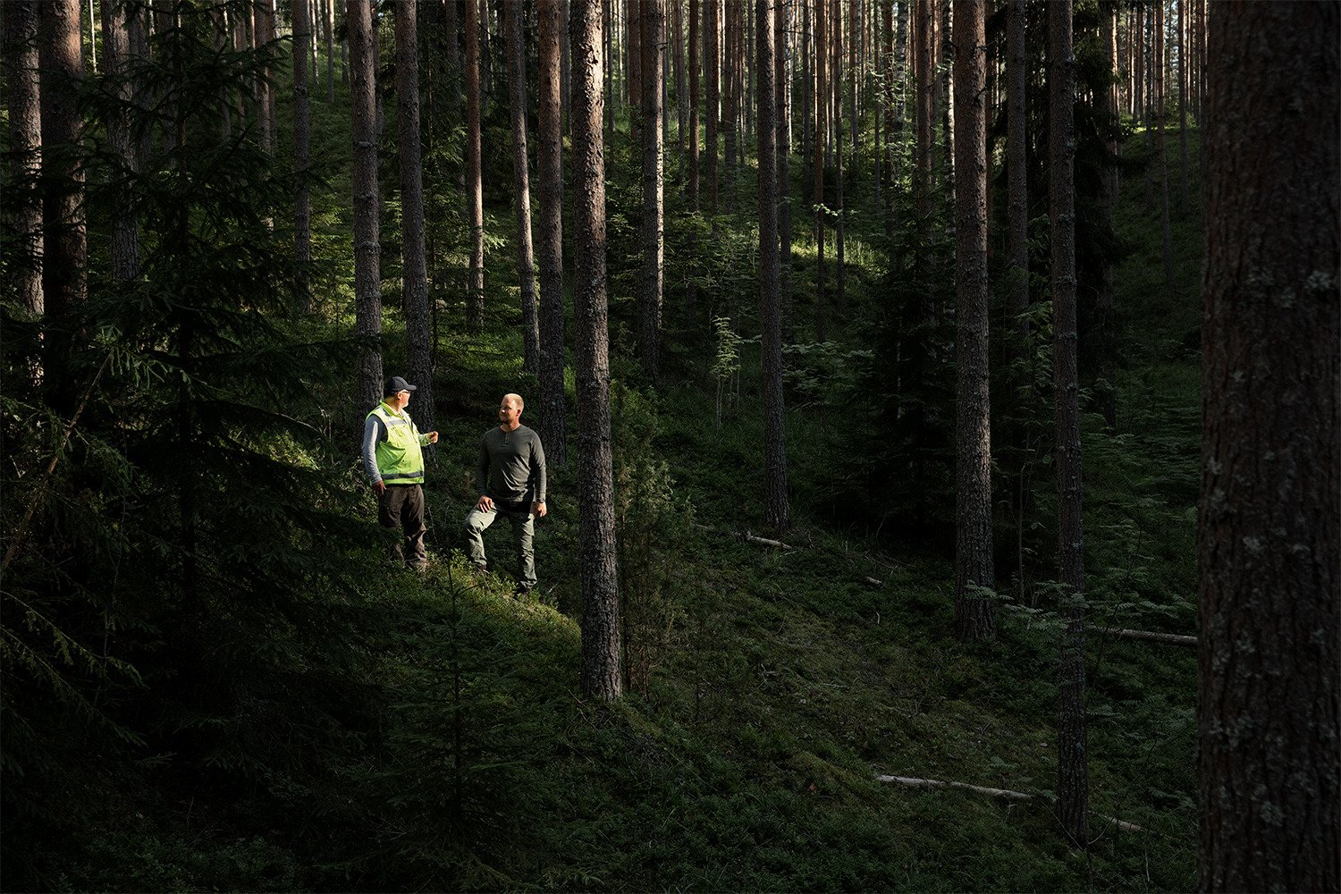 Kaksi henkilöä metsäisessä rinteessä.