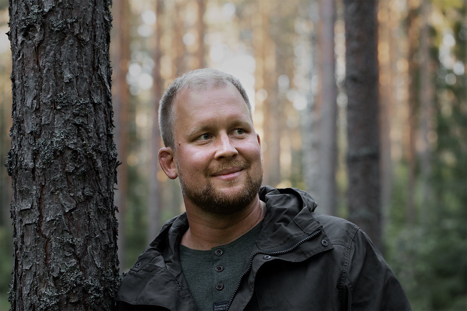 Henkilö hymyilee metsässä.