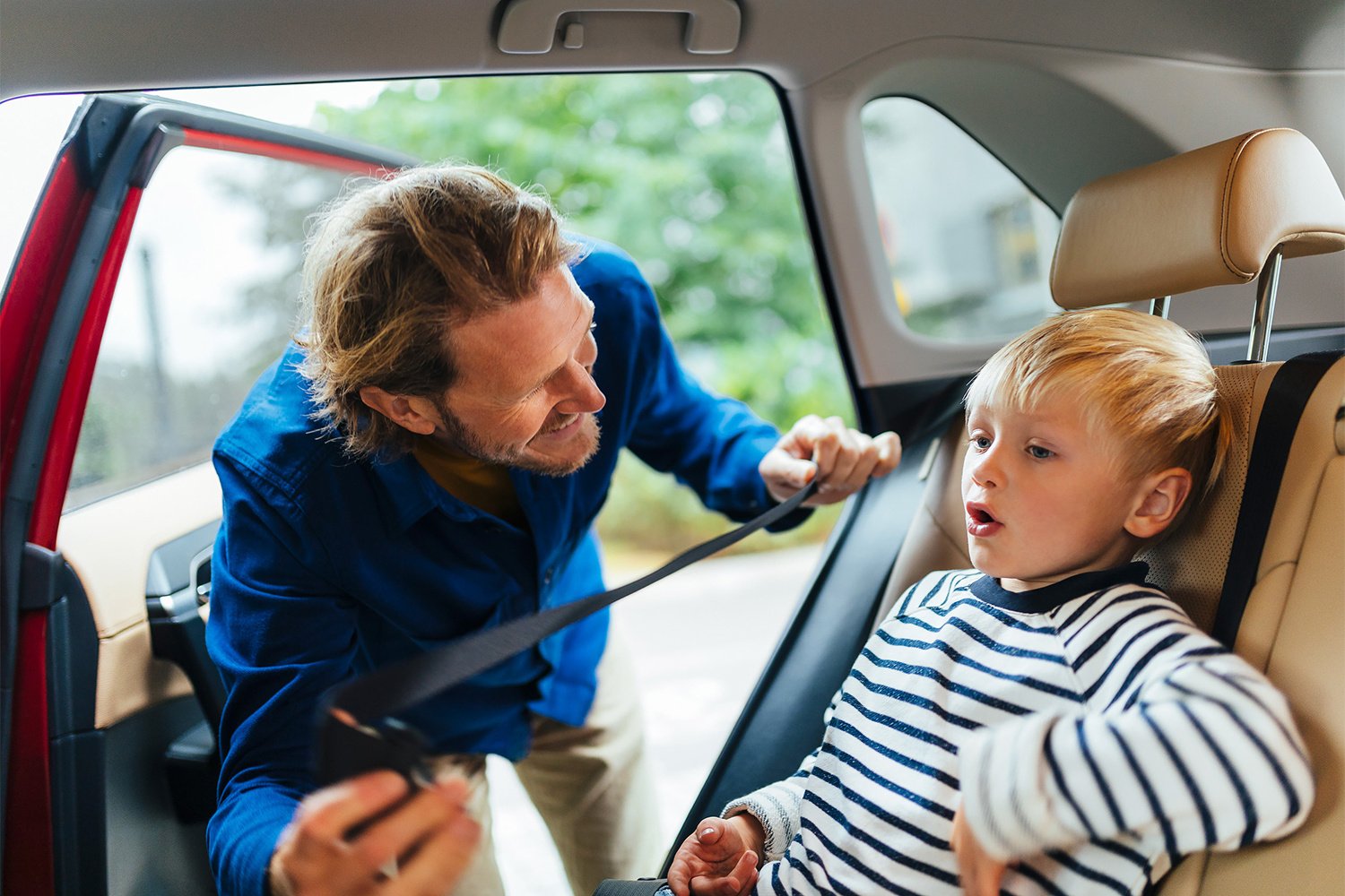 Aikuinen laittaa lapselle turvavyötä autossa.